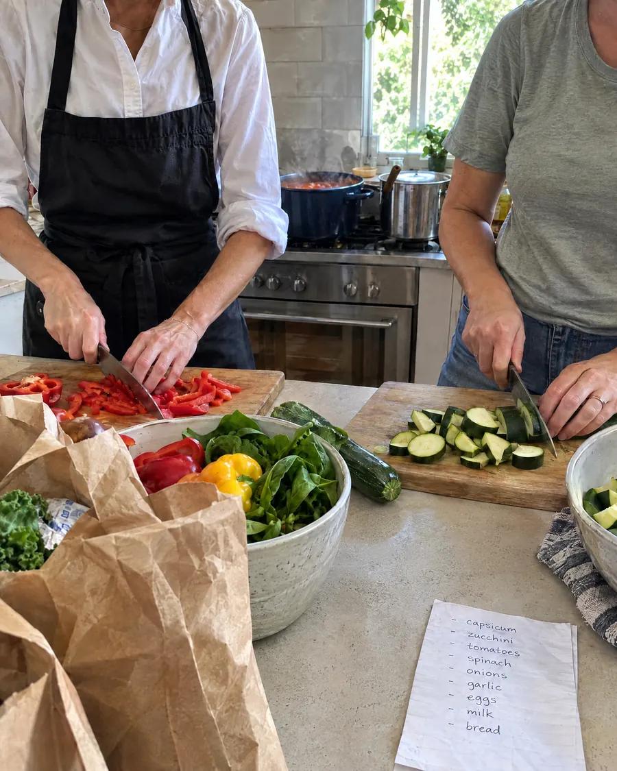 A chef and a client chopping vegetables side by side in a home kitchen